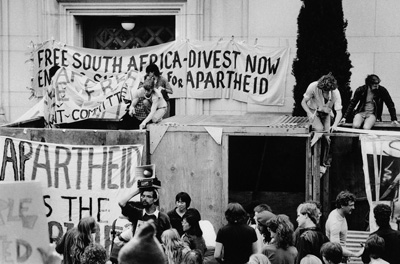 Março de 1986, Universidade da Califórnia em Berkeley. Os estudantes erguem barricadss para bloquearem as entradas do California Hall e exigirem que a universidade deixe de colaborar com a África do Sul